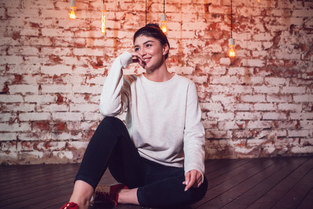 Attractive brunette in gray sweatshirt sits on brick wall background.