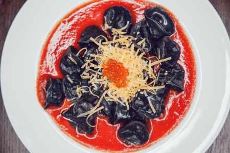 Black ravioli with salmon in tomato sauce decorated with cheese and red caviar.の写真素材