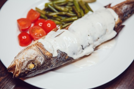 Grilled sea bass served on a plate with various sauces and and vegetablesの写真素材