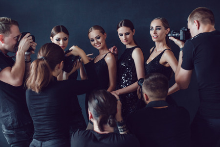 Photographers paparazzi take photos of women in cocktail dresses on dark background.の写真素材