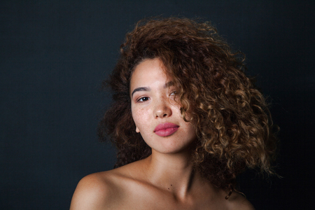Portrait of a curly woman with freckles and naked shoulders on dark background.の写真素材