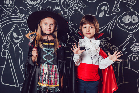 Children in scary Hallowe'en costumes stand against a wall with drawings. Witches and dracula.の写真素材