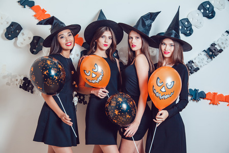 Women in witch halloween costumes standing with orange and black balloons on white background.の写真素材
