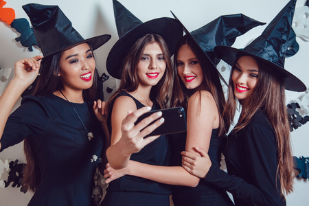 Women in witch halloween costumes standing and make selfie on white background.の写真素材