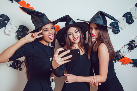 Women in witch halloween costumes standing and make selfie on white background.の写真素材