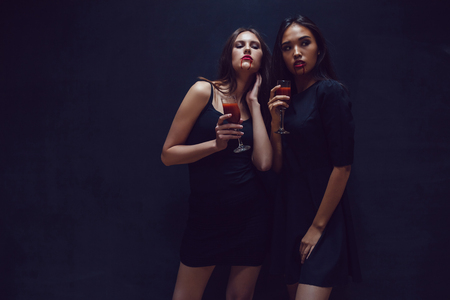 Attractive girls in the image of vampires hold glasses with blood. Halloween.の写真素材