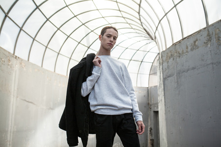 Stylish young man in gray sweatshirt on building background. Mock-up.