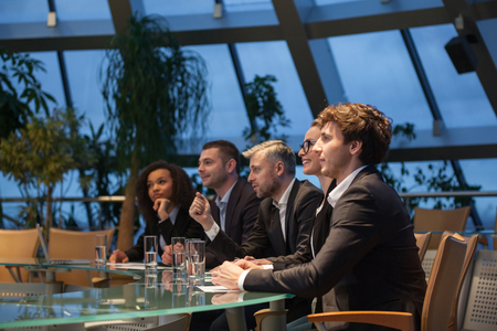 A group of business people sit at a table in a line and are discussing.