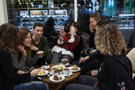 Group of positive teens use a smartphone and spend time in a cafe.の写真素材