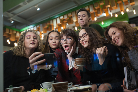 Group of positive teenagers make selfies and spending time in a cafe.の写真素材