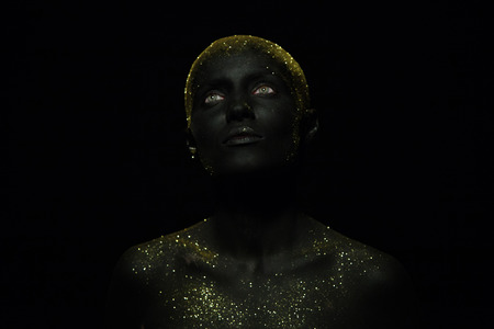 Portrait of a beautiful woman with creative body art glowing make up. Face is colored with black paint.の写真素材