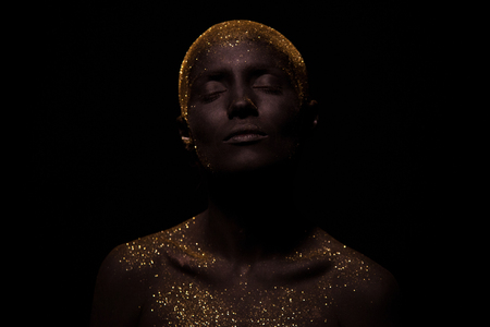 Portrait of a beautiful woman with creative body art glowing make up. Face is colored with black paint.の写真素材