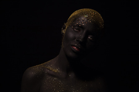 Portrait of a beautiful woman with creative body art glowing make up. Face is colored with black paint.の写真素材