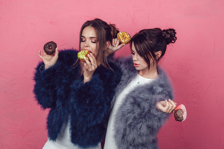Beautiful girls with donuts posing on pink background.の写真素材