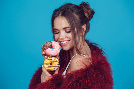 Attractive young woman in bright fur coat posing with donuts in hands.の写真素材