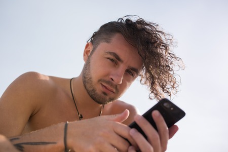 A man with curly hair uses a smartphone.の写真素材