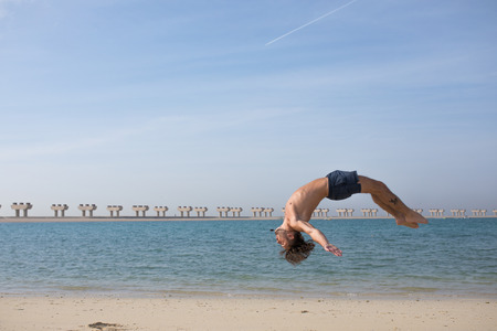 Young man doing somersault on the beach.の写真素材
