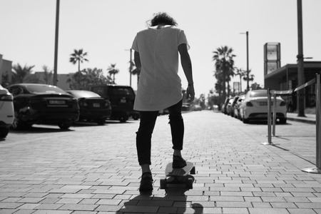 A young man in a white t-shirt riding a skateboard on the street.の写真素材