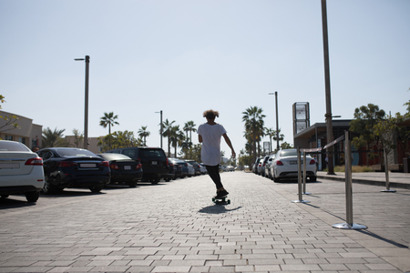 A young man in a white t-shirt riding a skateboard on the street.の写真素材
