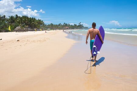 Mirissa/Sri Lanka - April 9, 2018: Male surfer walking along the shore with a surfboard.