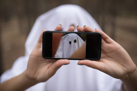 Woman in halloween ghost costume make selfie in the forest.の写真素材