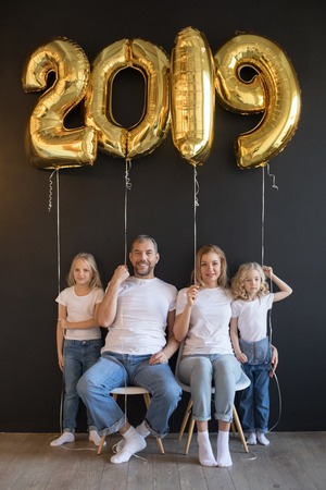 Happy family holding sign 2019 made of golden balloons for new year on black background.の写真素材