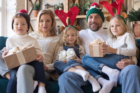 Happy family in funny Christmas hats hold presents and sit on the sofa.の写真素材
