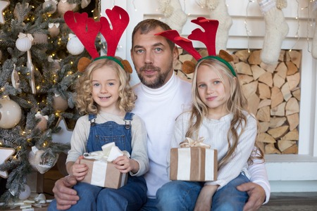 Dad is sitting with two daughters near the Christmas tree.の写真素材
