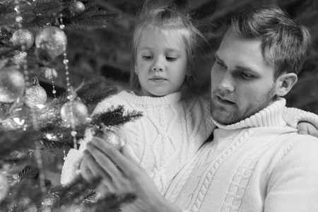 Dad keeps daughter in his arms and decorate christmas tree.の写真素材