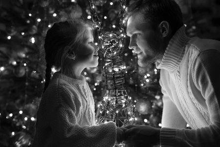 Father and daughter sit near the Christmas tree with decorative deer.の写真素材