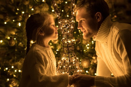 Father and daughter sit near the Christmas tree with decorative deer.の写真素材