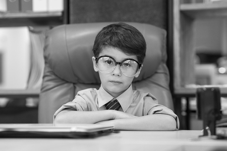 Little businessman in glasses sits in an office chair.の写真素材