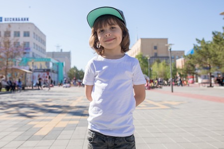 Cute little boy in a white t-shirt walks down the street.の写真素材