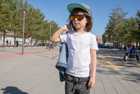 Cute little boy in a white t-shirt walks down the street.の写真素材
