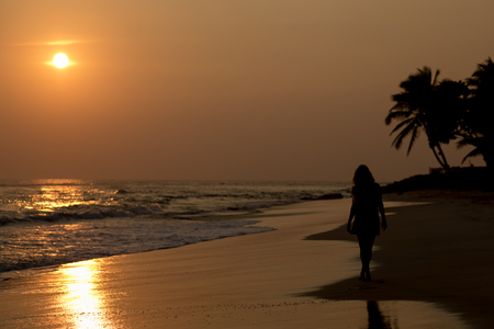 Female silhouette walking along the beach against the backdrop of a beautiful sunset.の写真素材