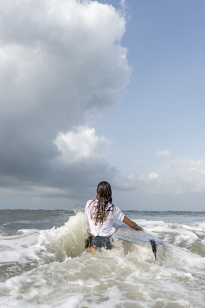 Woman surfer in white t-shirt walks into the ocean with board.の写真素材