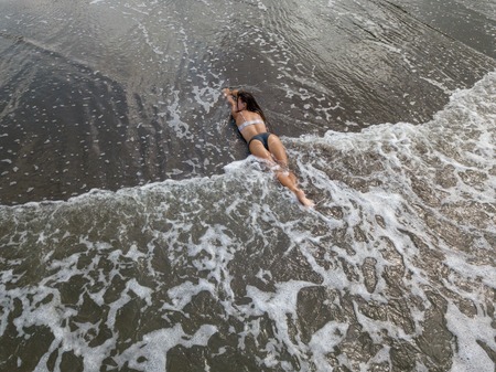 Top view of a woman lying on the beach with black sand, foaming waves of ocean.の写真素材