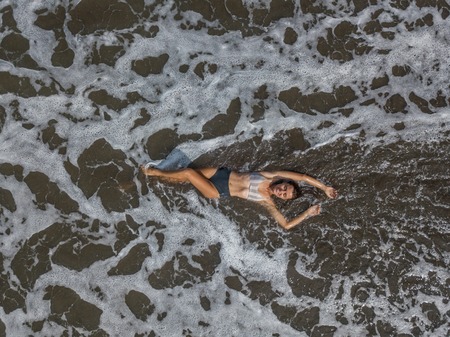 Top view of a woman lying on the beach with black sand, foaming waves of ocean.の写真素材