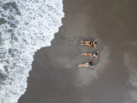 Top view of a women lying on the beach with black sand, foaming waves of ocean.の写真素材