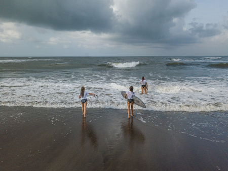 Women surfers walk along the black beach.の写真素材