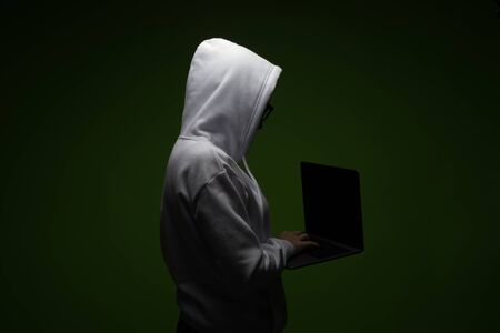 A woman in a hood is using a laptop. Hacker is using a laptop.