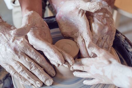 Potter's hands guiding child's and woman's hands to help him to work with the pottery wheel.の写真素材