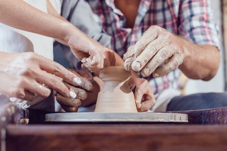 Potter's hands guiding child's and woman's hands to help him to work with the pottery wheel.の写真素材
