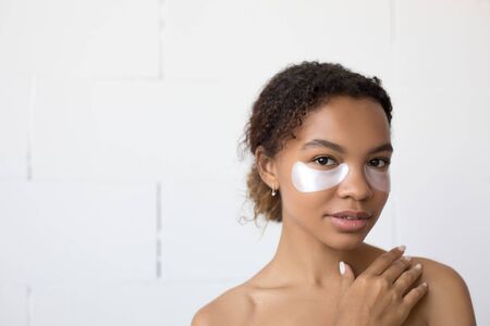 Young afro american woman with collagen pads under her eyes on white background.