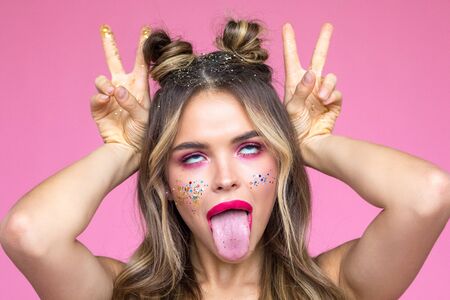 Girl with bright makeup grimaces and shows tongue. Glitter Makeup.
