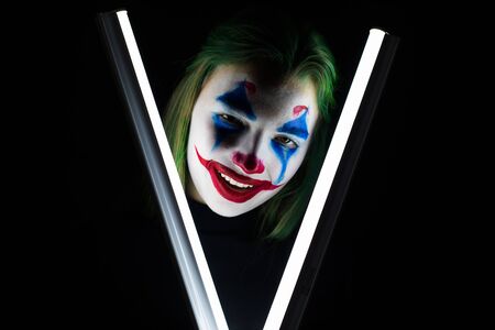 Portrait of a girl with clown makeup holds a glowing lamp on a black background.のeditorial素材