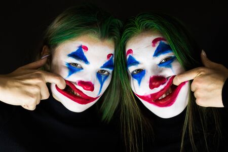 Portrait of two young women with clown makeup on black background.