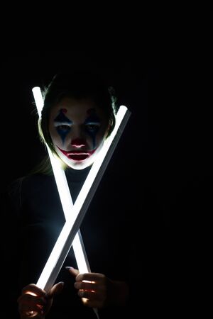 Portrait of a girl with clown makeup holds a glowing lamp on a black background.のeditorial素材