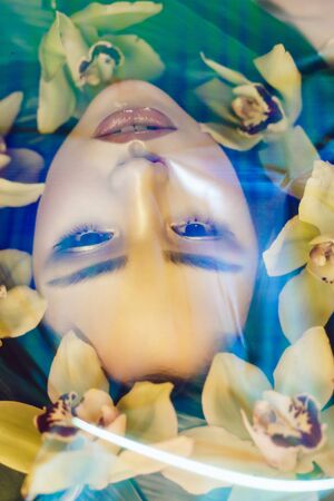 Portrait of beautiful girl with make-up and orchid flowers around her face. Woman and flowers. Spring.の写真素材