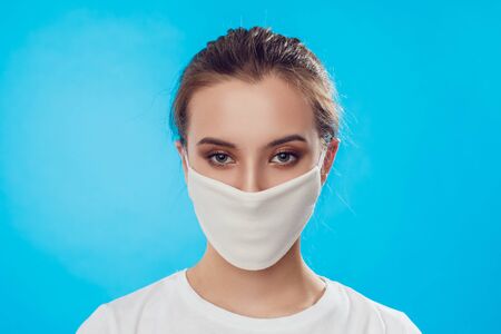 Woman wearing face protective mask on face against Coronavirus on the blue background. COVID-19 Pandemic.の写真素材